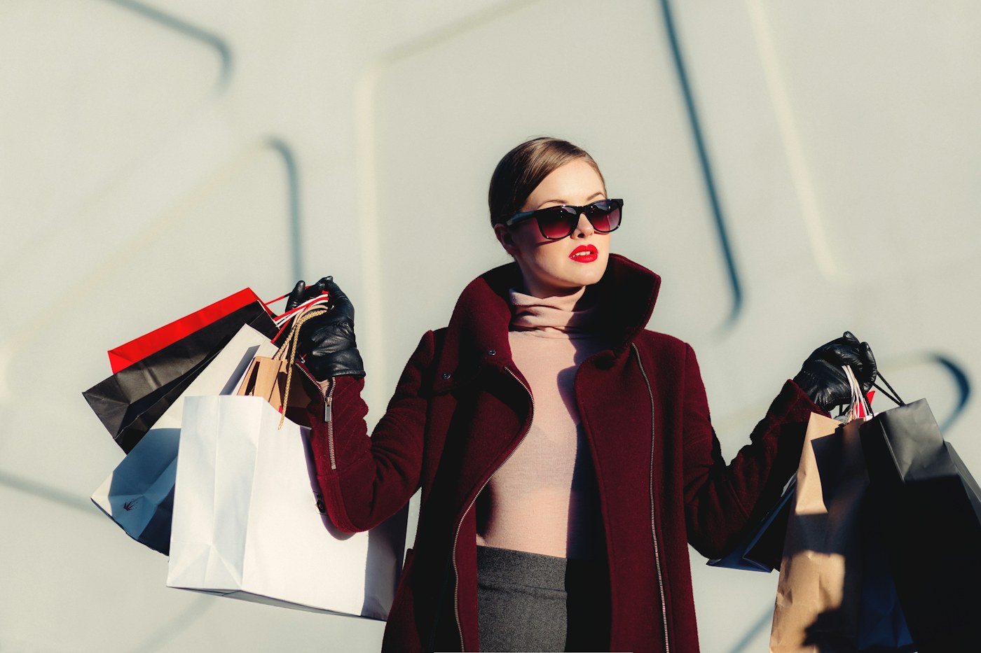 Woman in a coat and sunglasses holding shopping bags outdoors